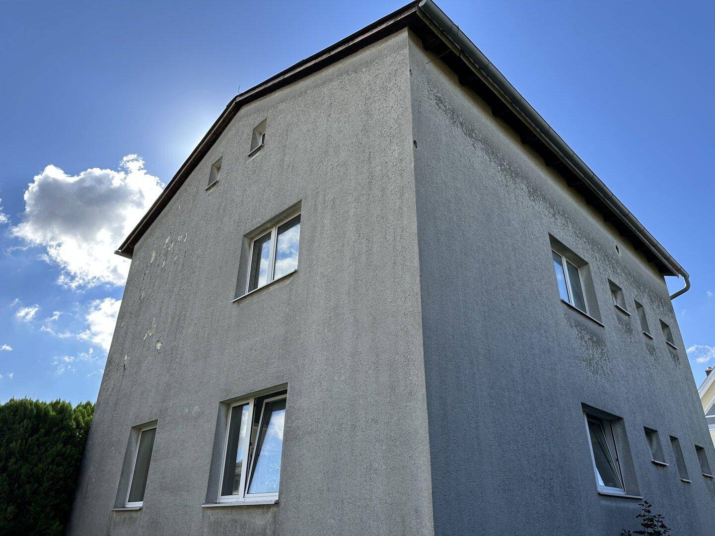 Eckansicht der Hausfassade mit Fenstern unter strahlend blauem Himmel und Sonnenschein.