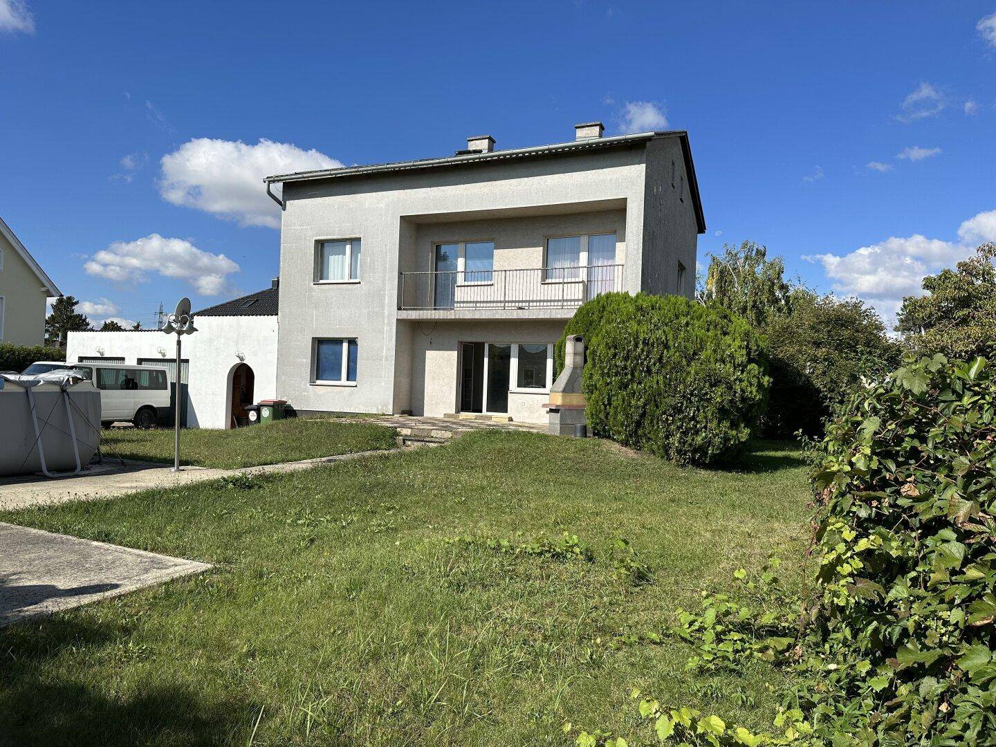 Vorderansicht eines Hauses mit Rasenfläche und einem kleinen Balkon unter blauem Himmel.