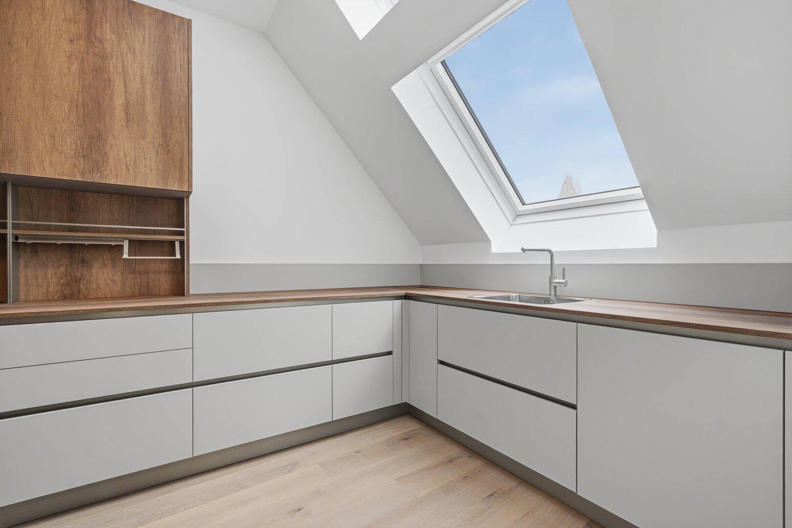 Moderne Küche mit Holz-Arbeitsplatten, hellgrauen Schränken und großem Dachfenster für viel Licht.
