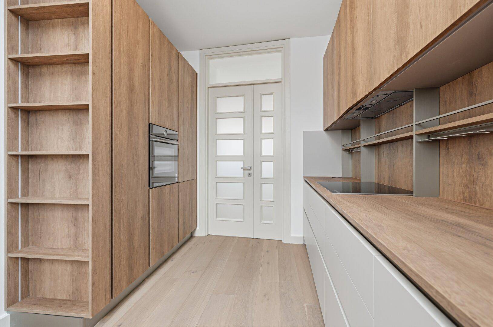 Stilvolle Küche mit hohen Holzschränken, integriertem Backofen und hellem Holzboden.