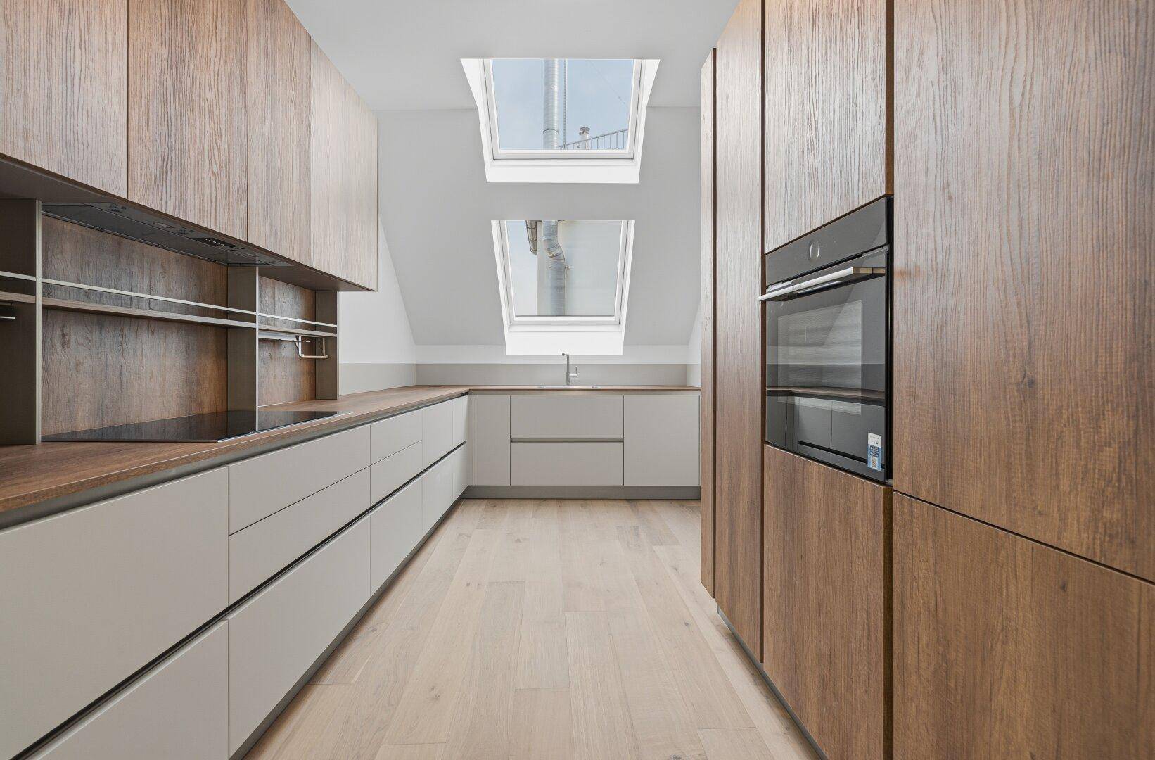 Helle, moderne Küche mit Holzfronten, integrierten Geräten und zwei Dachfenstern.