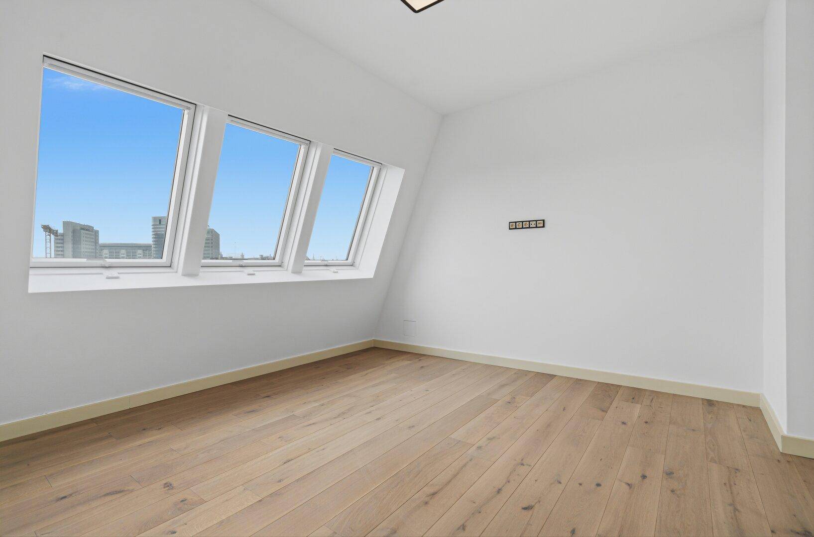 Helles Zimmer im Dachgeschoss mit schrägen Fenstern und Holzboden, bietet einen weiten Blick.