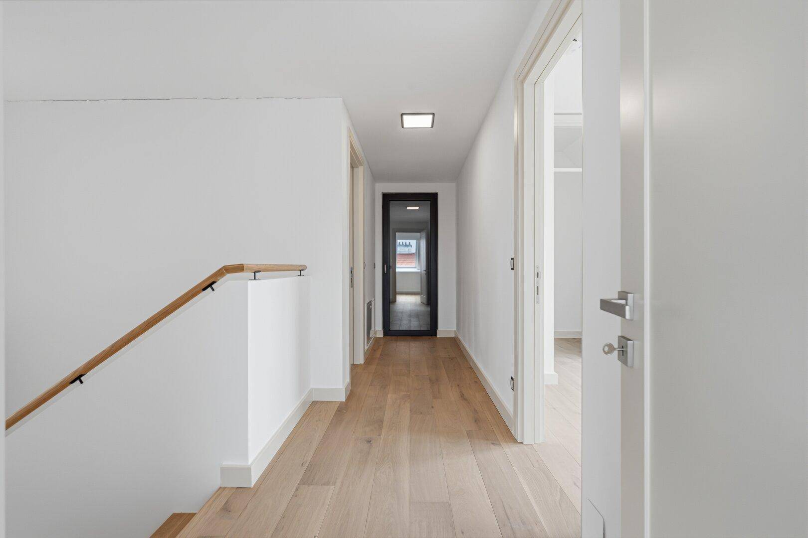 Heller Flur mit Holztreppe und Parkettboden, der zu weiteren Räumen führt.