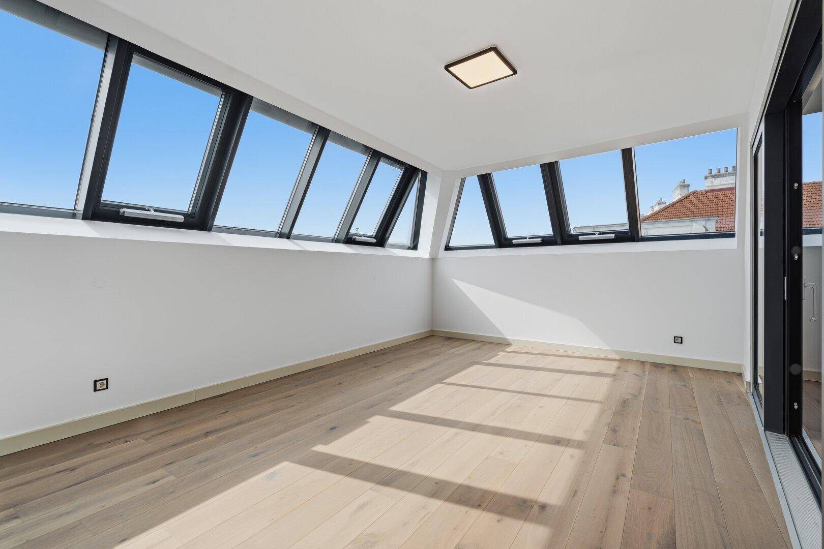 Geräumiger, heller Raum mit Holzboden und mehreren Dachschrägenfenstern für viel Tageslicht.