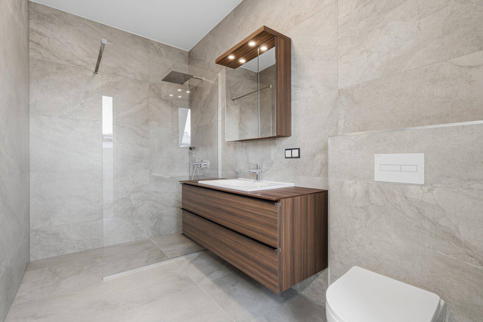 Modernes Badezimmer mit begehbarer Dusche, schwebendem Waschtisch und grauen Fliesen.