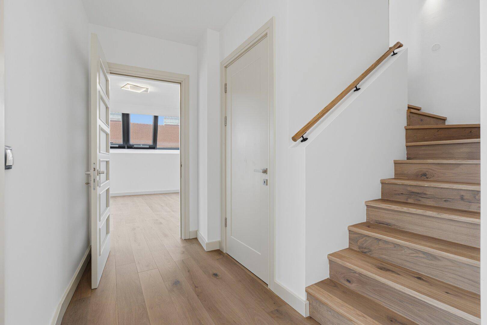 Heller Flur mit Holzboden und einer eleganten Holztreppe, die in die obere Etage führt.