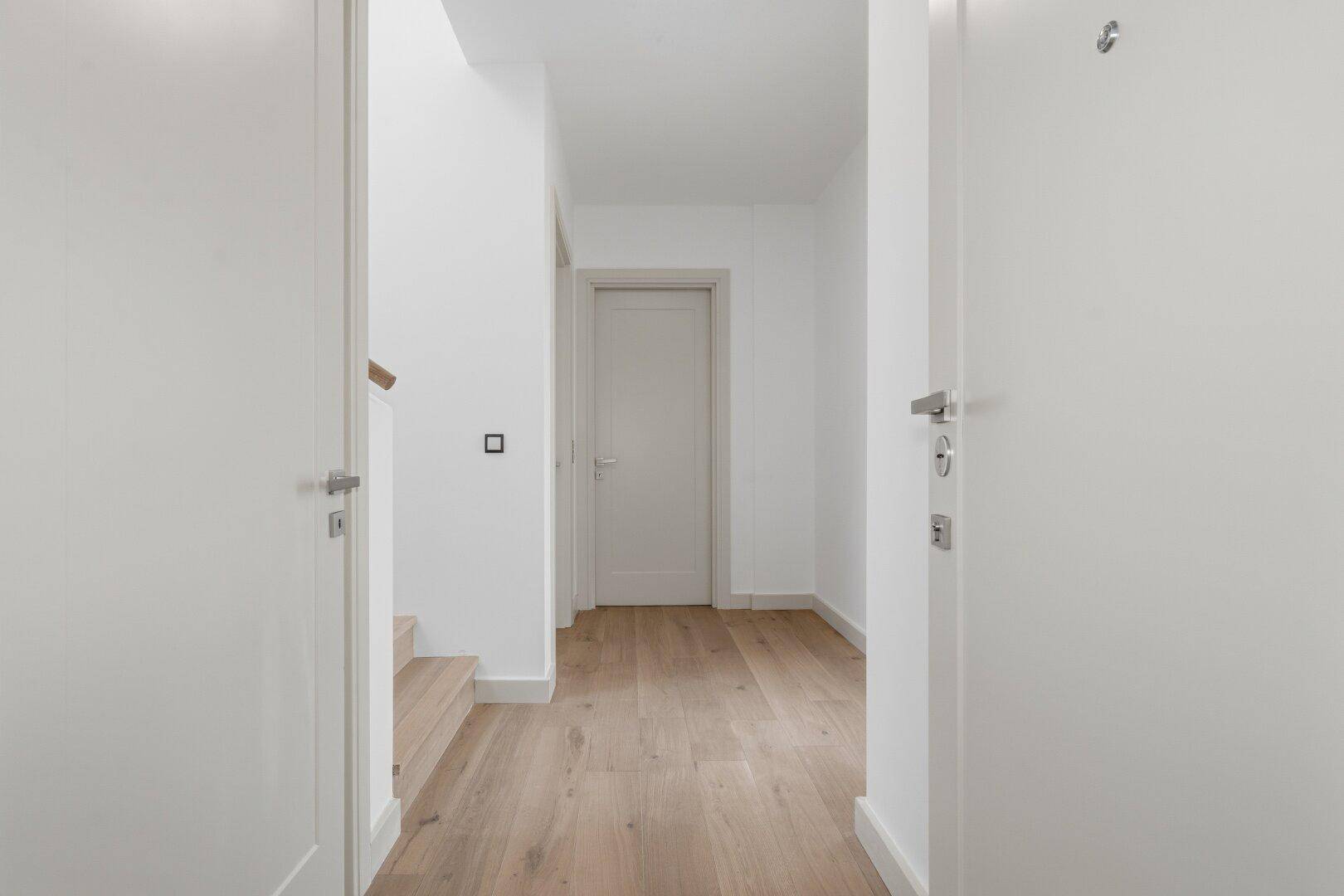 Heller Flur mit Holzboden und weißen Türen, der zu weiteren Räumen führt.