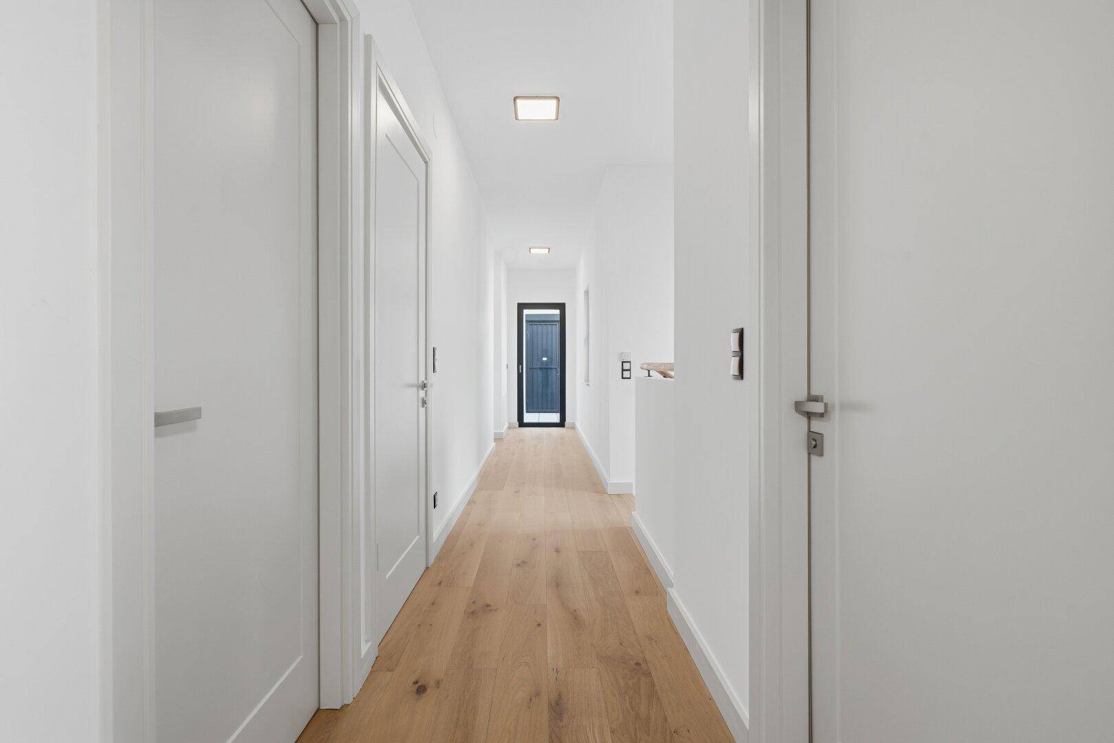 Langer, heller Flur mit Holzboden und weißen Türen, der zu den verschiedenen Wohnbereichen führt.