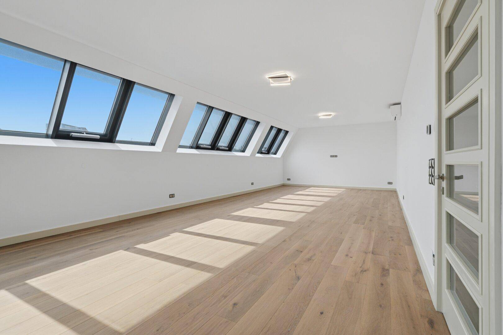 Geräumiger, leerer Wohnbereich mit hellen Holzböden und schrägen Dachfenstern, bereit zur individuellen Gestaltung.