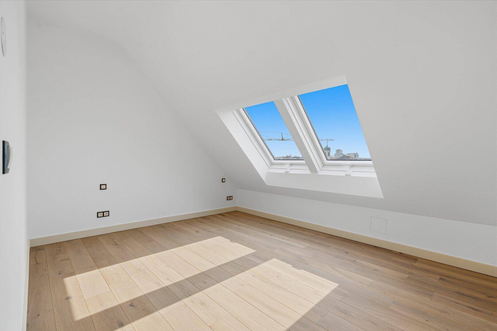 Helles, leeres Zimmer mit Holzboden und Dachfenstern, ideal als Kinderzimmer oder Gästezimmer.