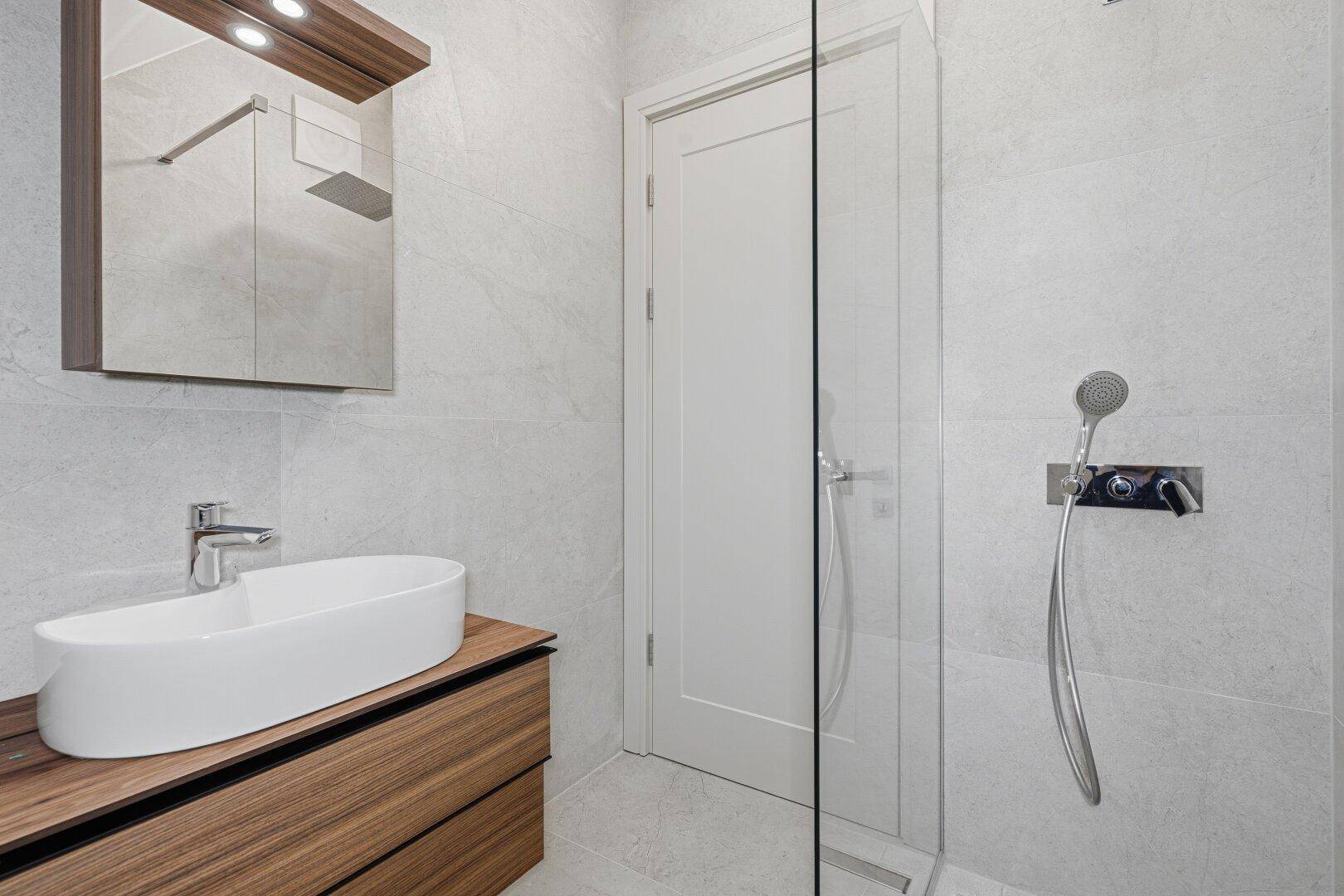 Modernes Badezimmer mit Einzelwaschbecken auf Holzunterschrank und einer begehbaren Dusche mit Glasabtrennung.