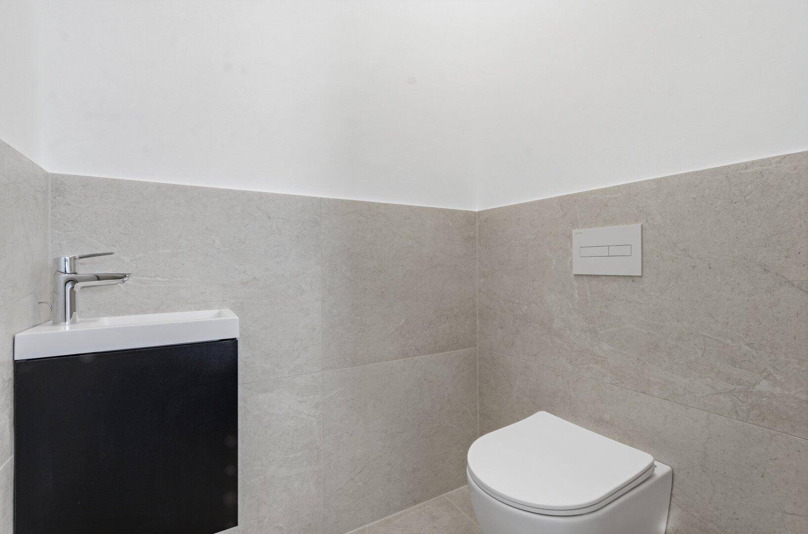 Kleines Gäste-WC mit wandhängender Toilette und modernem Eckwaschbecken mit schwarzem Unterschrank.