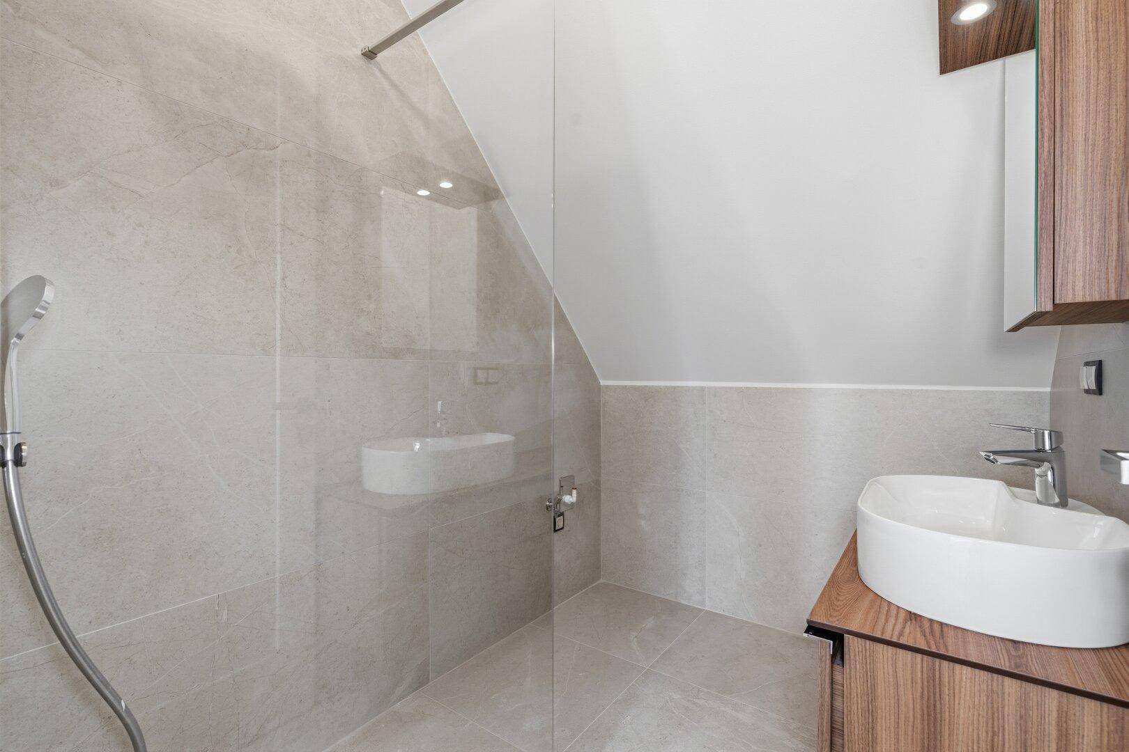Helles Badezimmer mit begehbarer Dusche, modernem Waschbecken und schräger Decke im Dachgeschoss.