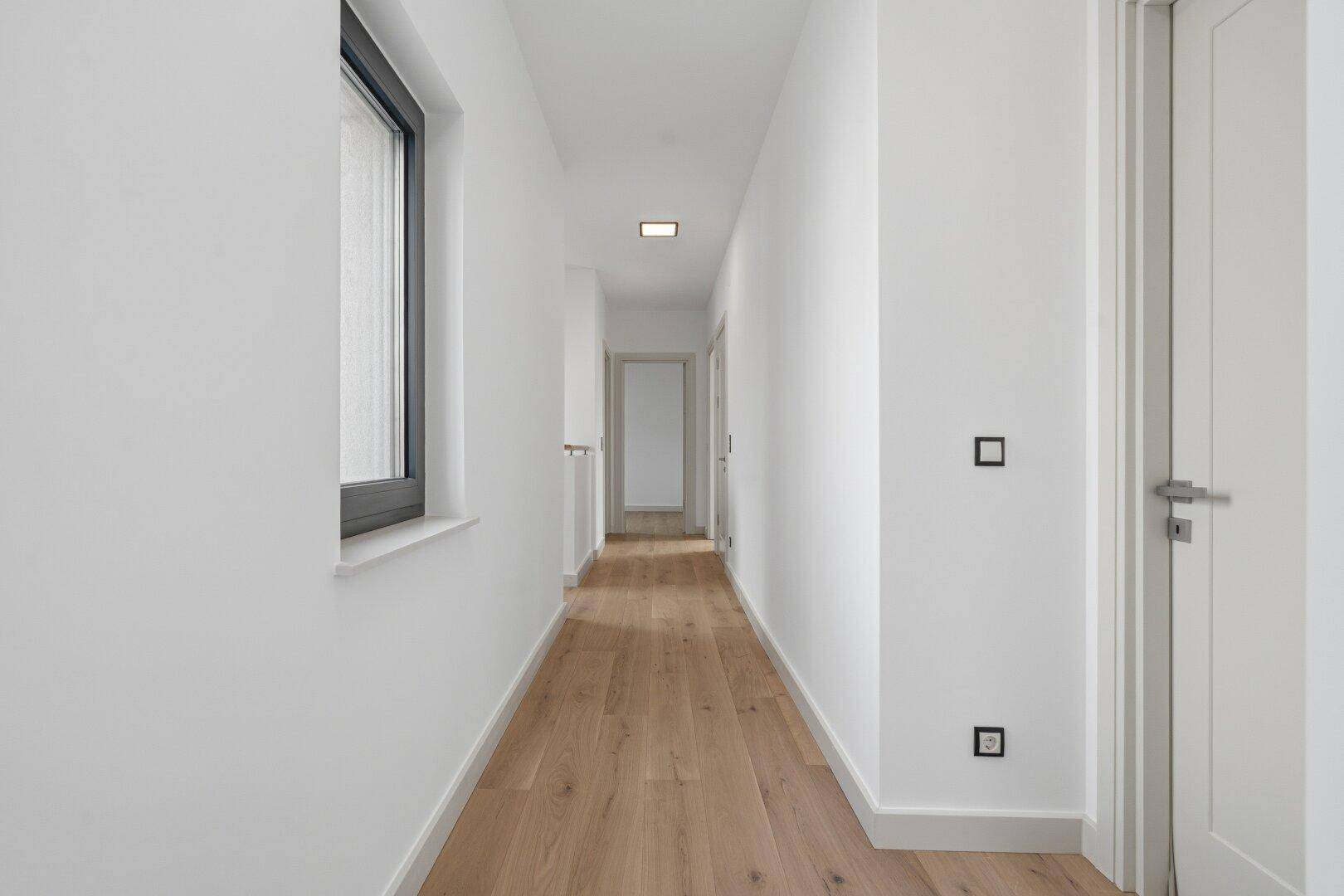 Langer, heller Flur mit Holzboden und Fenster, der zu verschiedenen Räumen führt.
