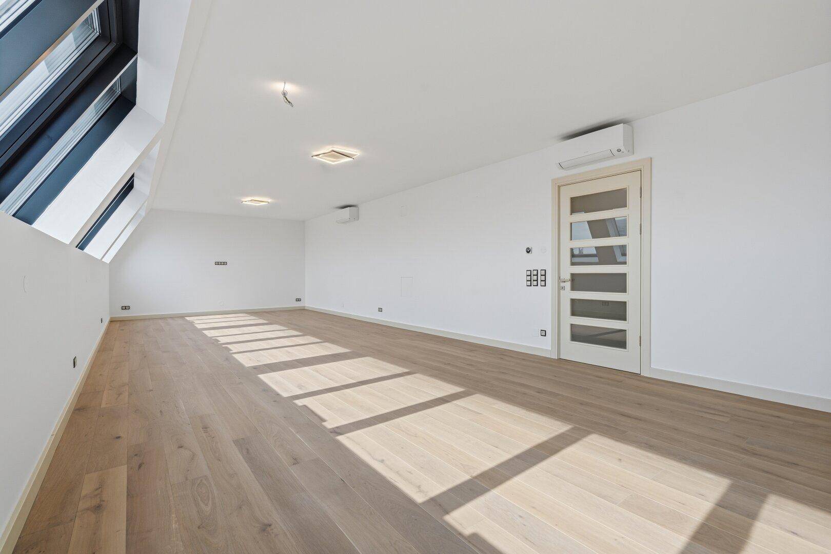 Heller, leerer Raum mit Holzboden und Dachschrägenfenstern, ideal für ein großzügiges Wohnkonzept.