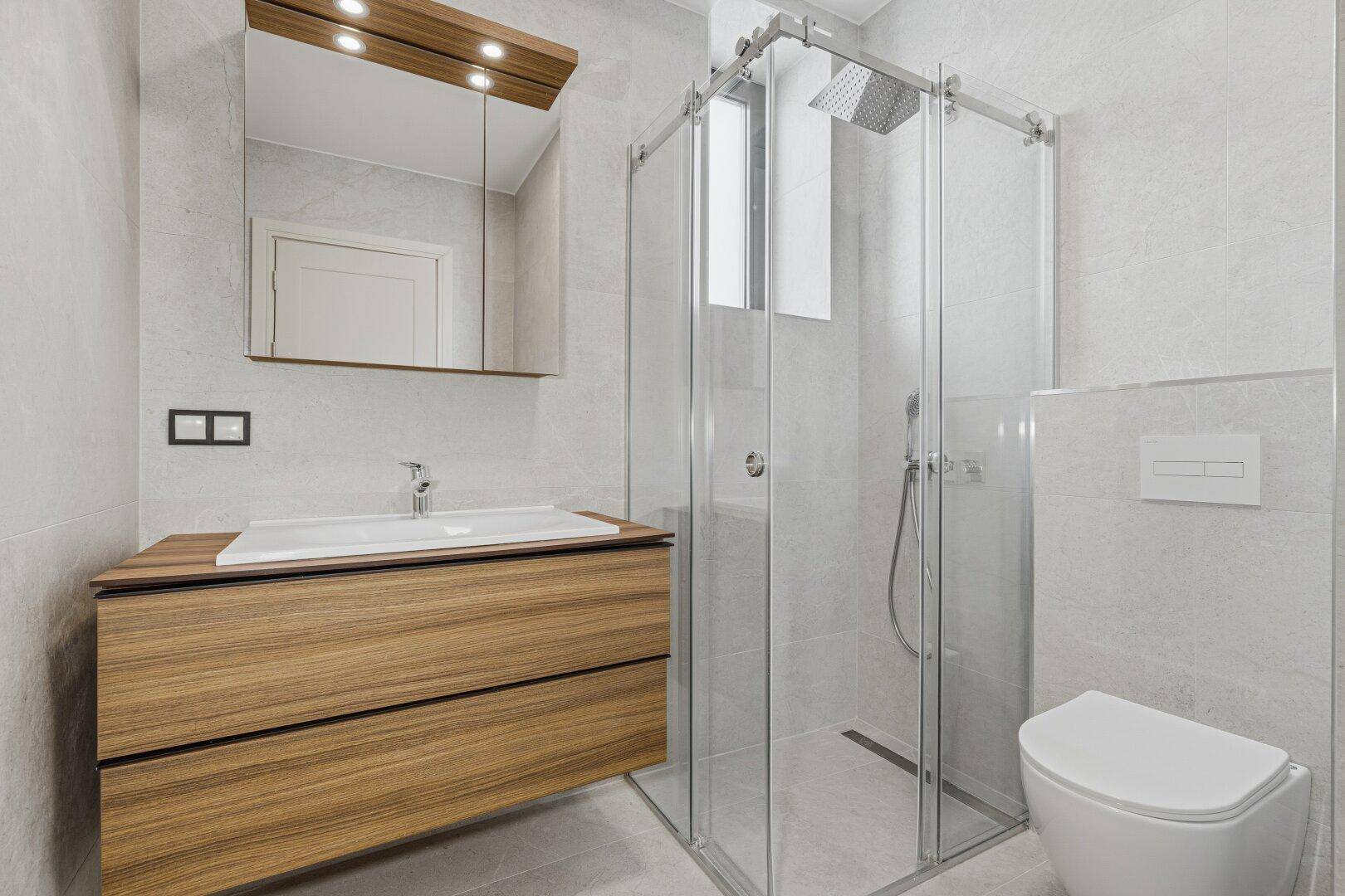 Zeitgemäßes Badezimmer mit großformatigen Fliesen, Holzwaschtisch und geräumiger Duschkabine.