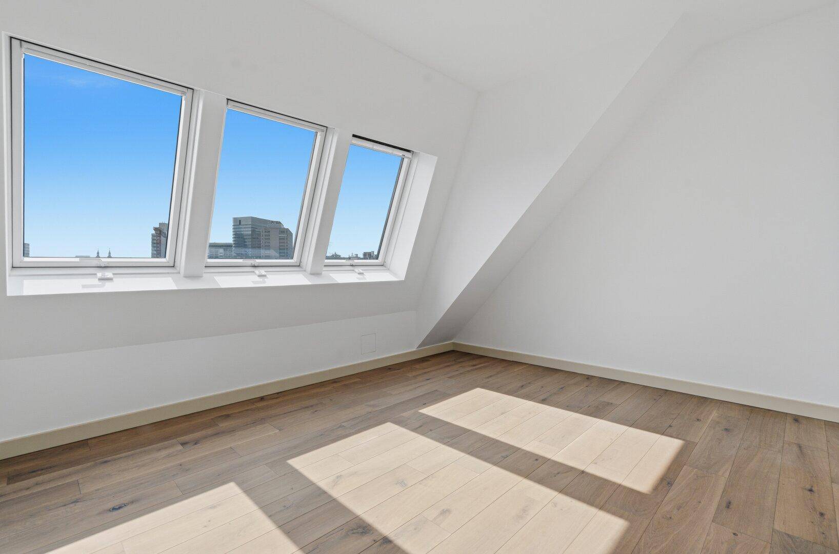 Helles, leeres Schlafzimmer mit Dachschrägenfenstern und Holzboden, bietet viel Tageslicht.