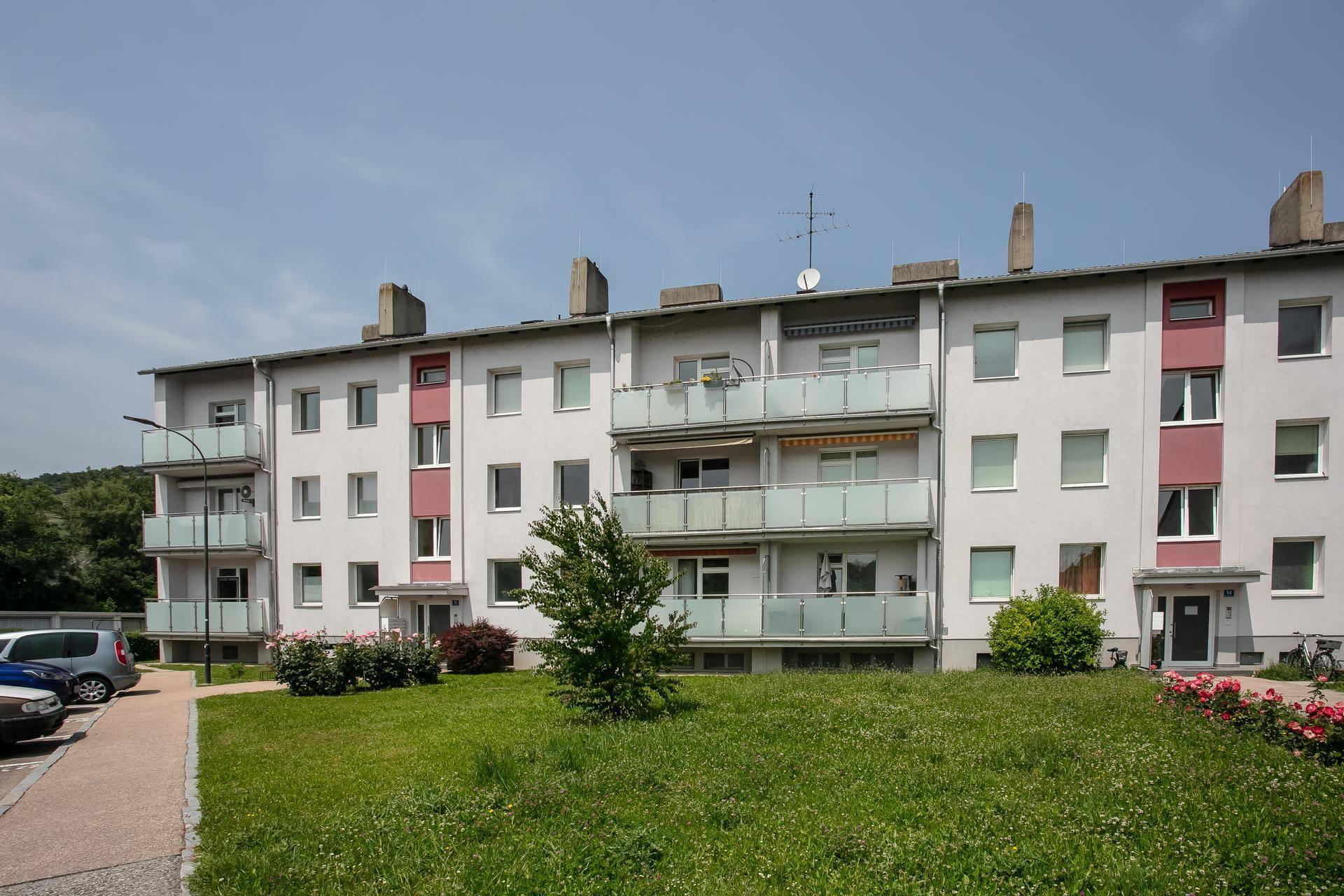 Mehrfamilienhaus mit Balkonen, gepflegter Grünfläche und Parkplätzen im Freien.
