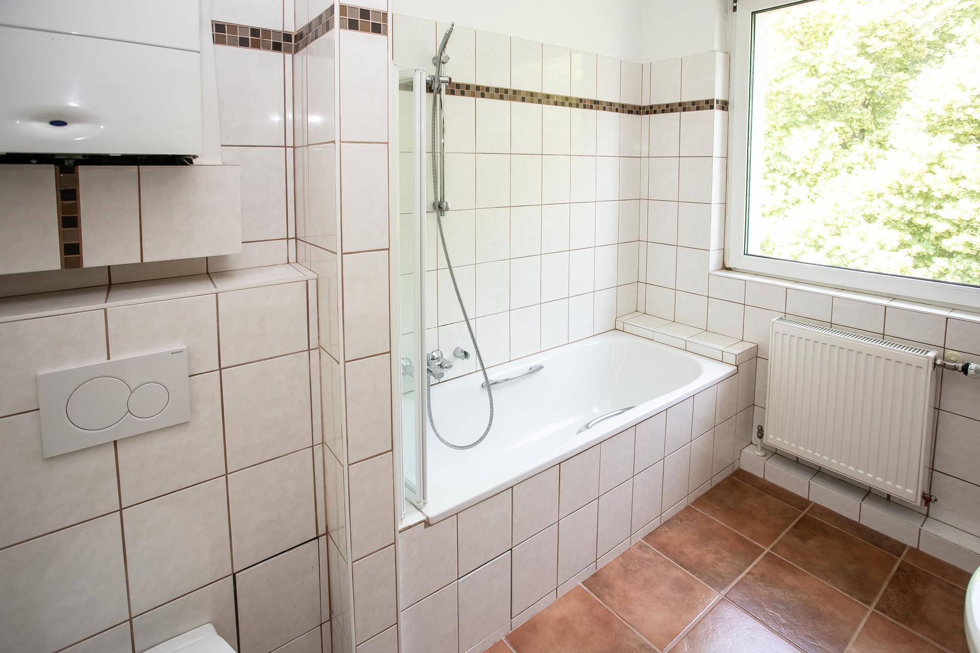Helles Badezimmer mit Badewanne, Duschvorrichtung und Fenster für Tageslicht.