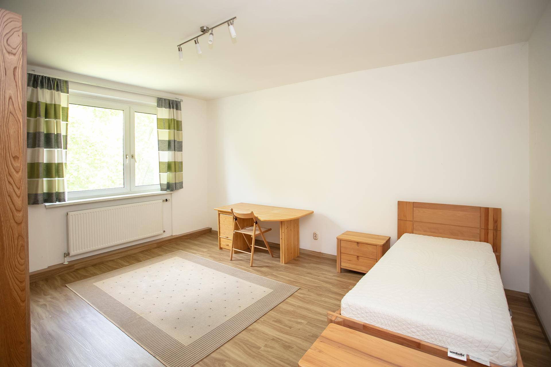 Schlafzimmer mit Holzbett, Schreibtisch und einem Fenster mit Blick ins Grüne.