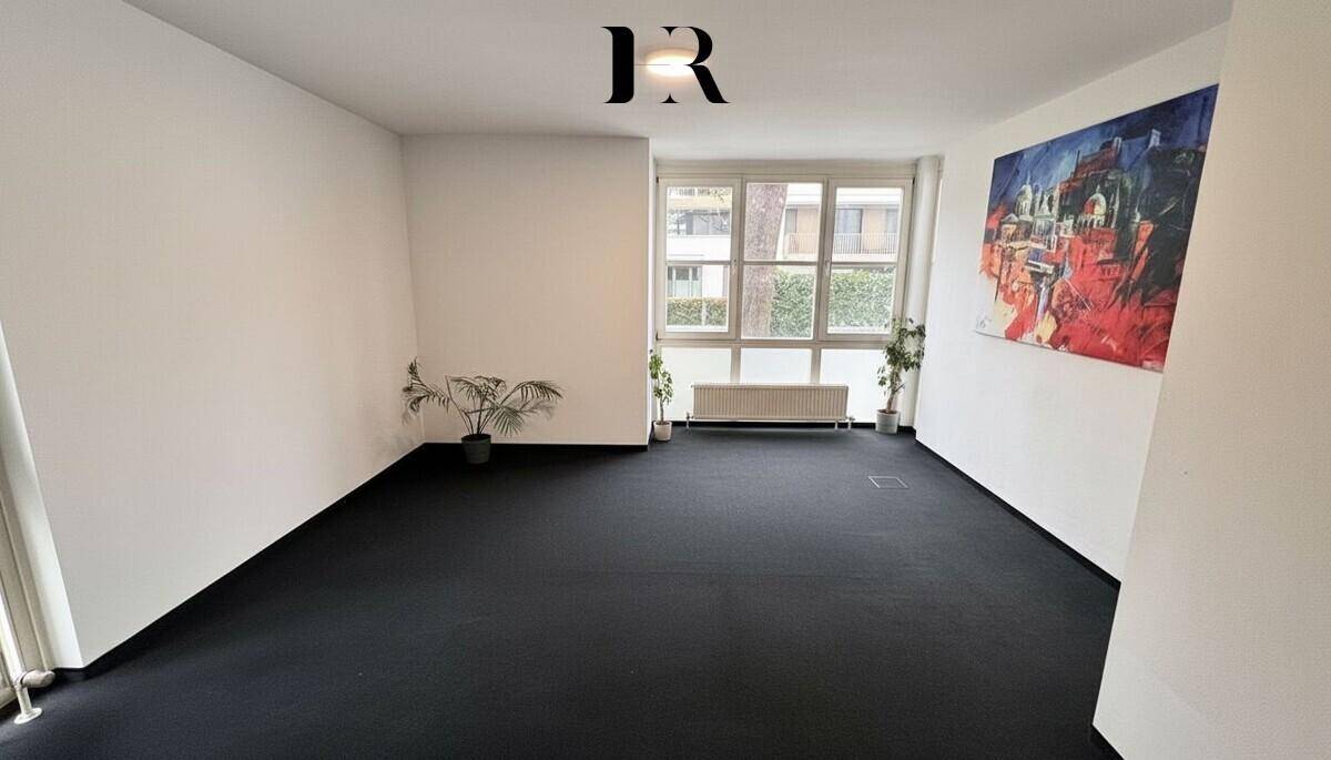 Unmöbliertes Schlafzimmer mit dunklem Teppichboden, weißen Wänden und großen Fenstern.