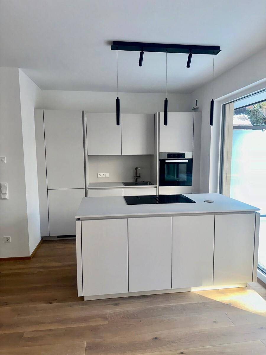 Helle, moderne Küche mit Kücheninsel, Induktionskochfeld und eleganten schwarzen Hängelampen.