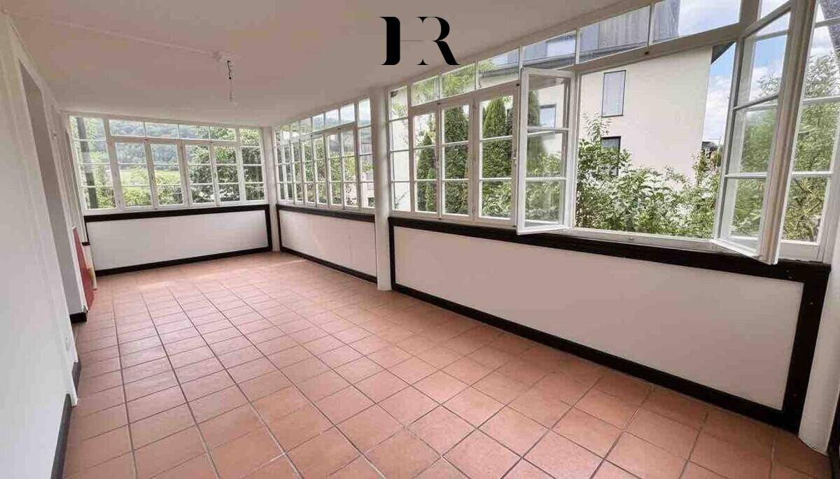 Heller Wintergarten mit vielen Fenstern und Fliesenboden, ideal für entspannte Stunden.