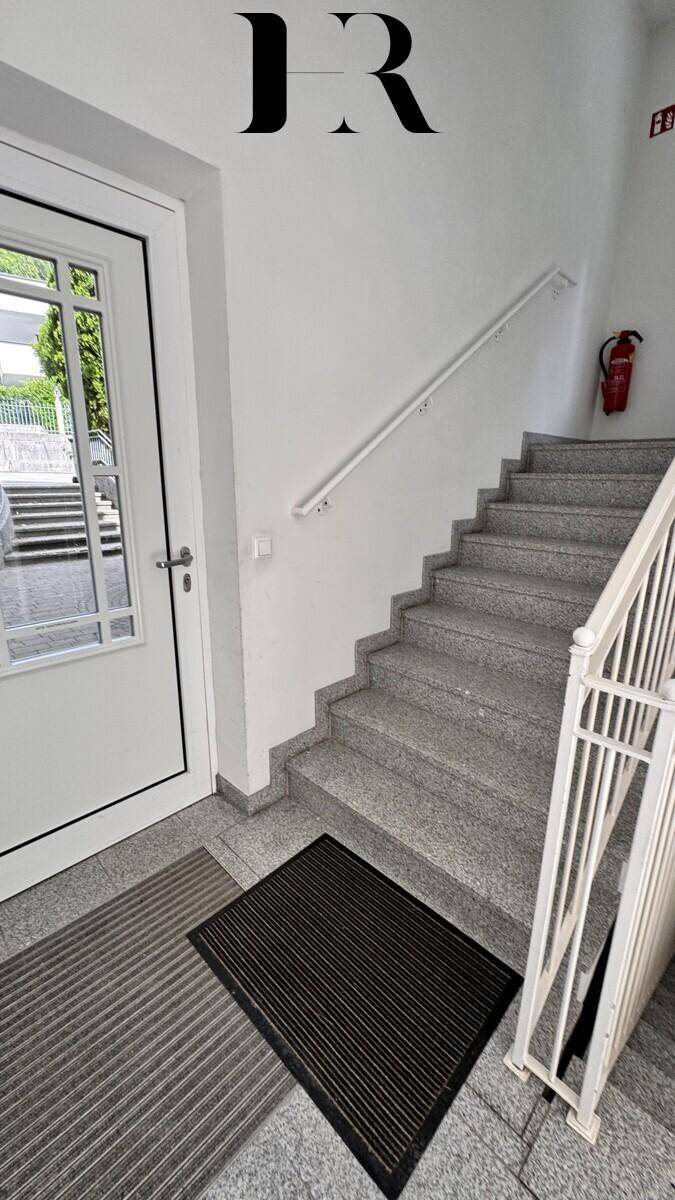 Heller Eingangsbereich mit Steintreppe und Handlauf, der zu den oberen Etagen führt.