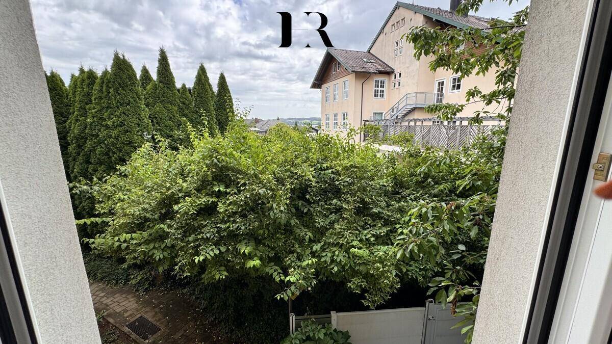 Blick aus dem Fenster auf üppiges Grün und ein charmantes Gebäude im Hintergrund.