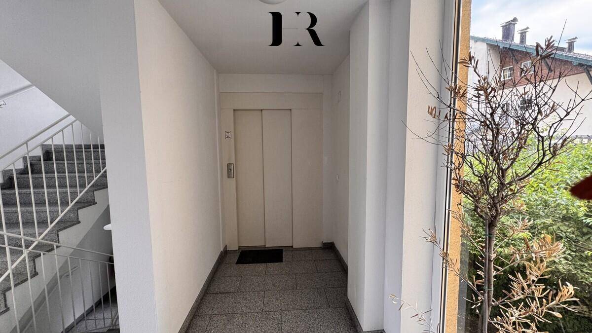Treppenhaus mit Aufzug und Fenster, das viel Tageslicht in den Flur bringt.