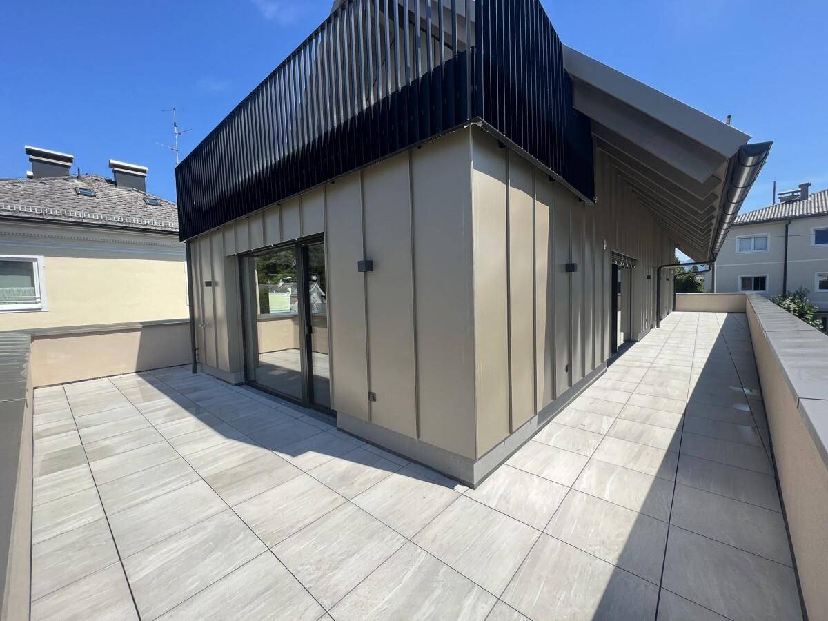 Weitläufige Dachterrasse mit modernen Fliesen und der Fassade des Gebäudes unter blauem Himmel.