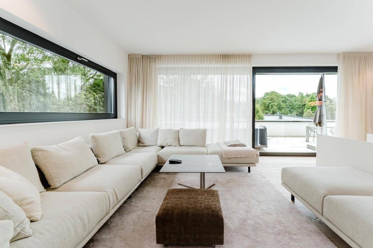 Helles Wohnzimmer mit großem Ecksofa, Teppichboden und Schiebetüren zur Terrasse.