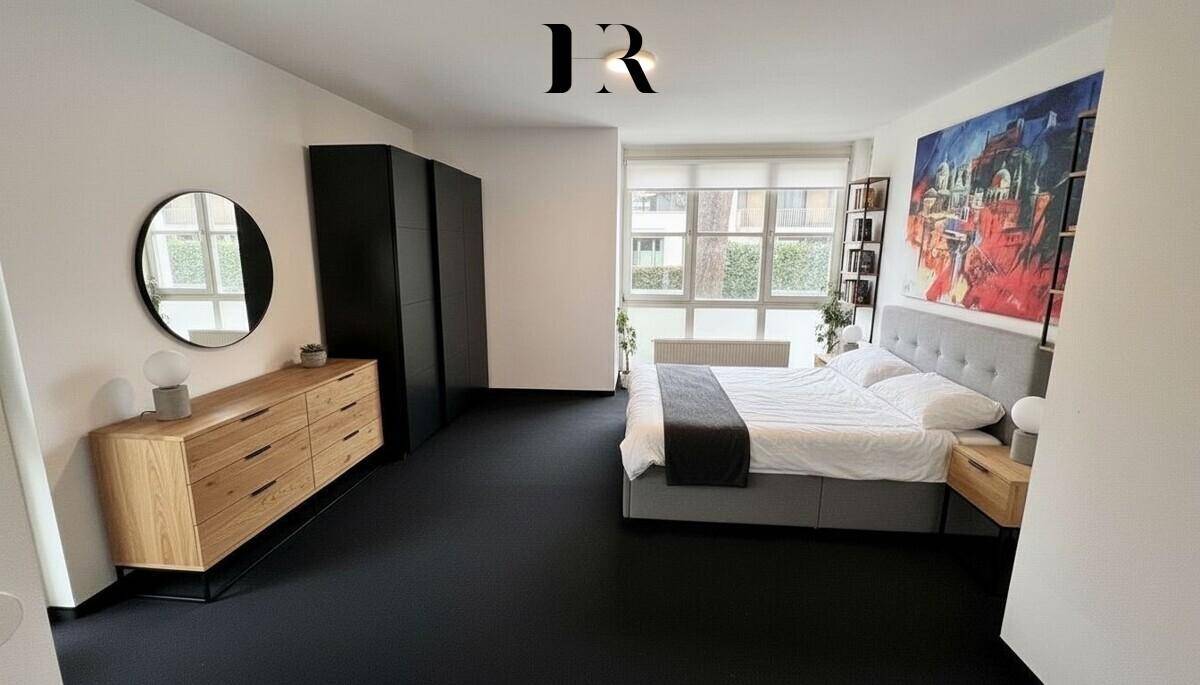 Modernes Schlafzimmer mit dunklem Teppichboden, großem Bett, Holzkommode und Einbauschränken.