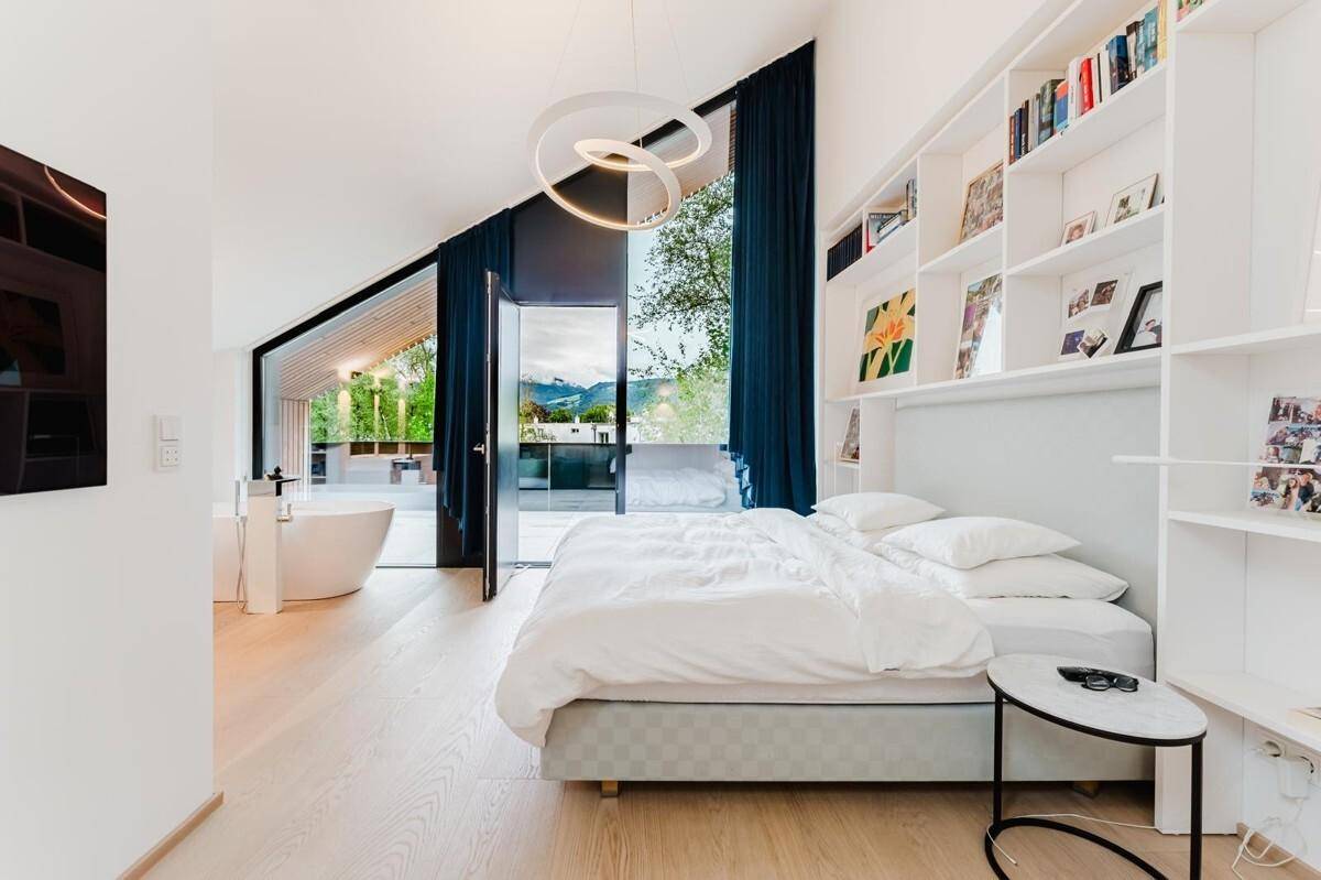 Helles Schlafzimmer mit freistehender Badewanne, Einbauregalen und Bergblick.