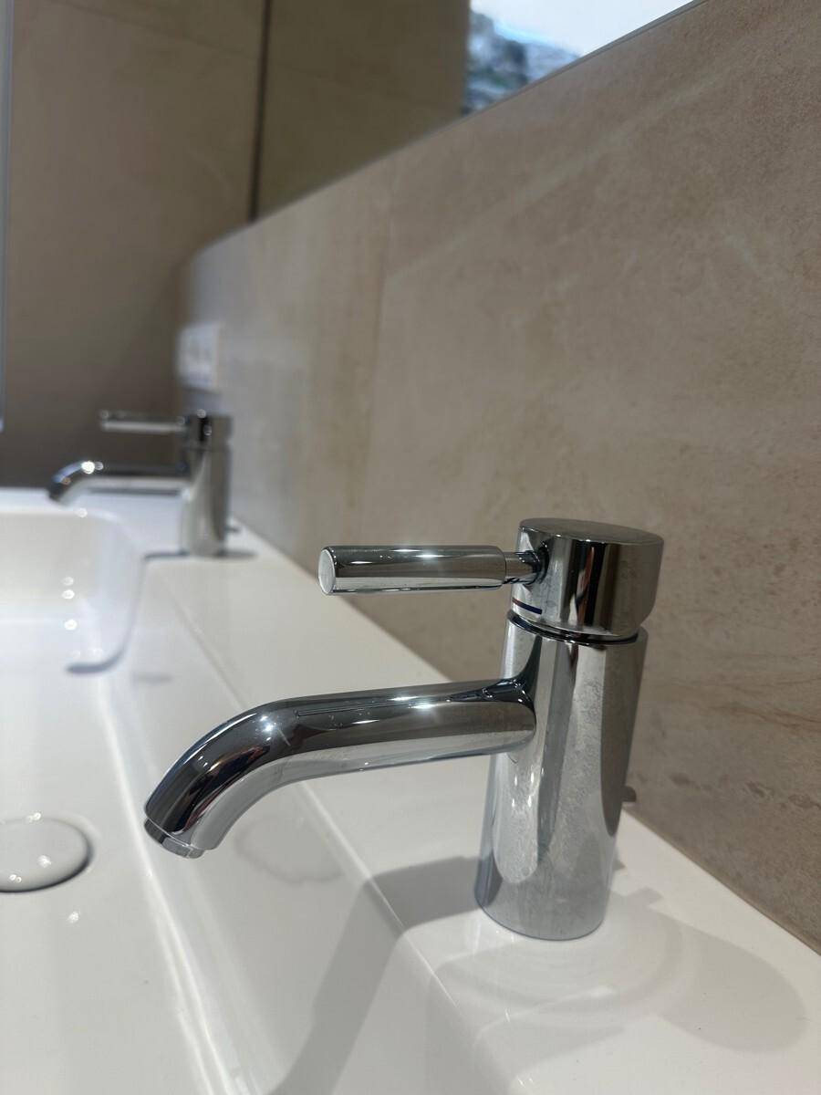 Nahaufnahme eines glänzenden, modernen Wasserhahns über einem weißen Waschbecken.