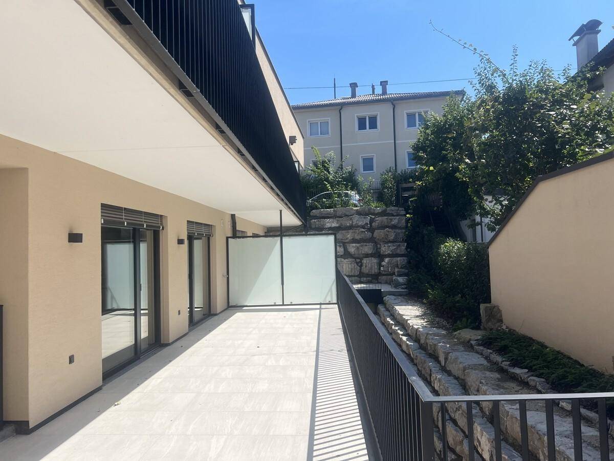 Untere Terrasse mit modernen Fliesen, Glasabtrennung und einer dekorativen Steinmauer im Hintergrund.
