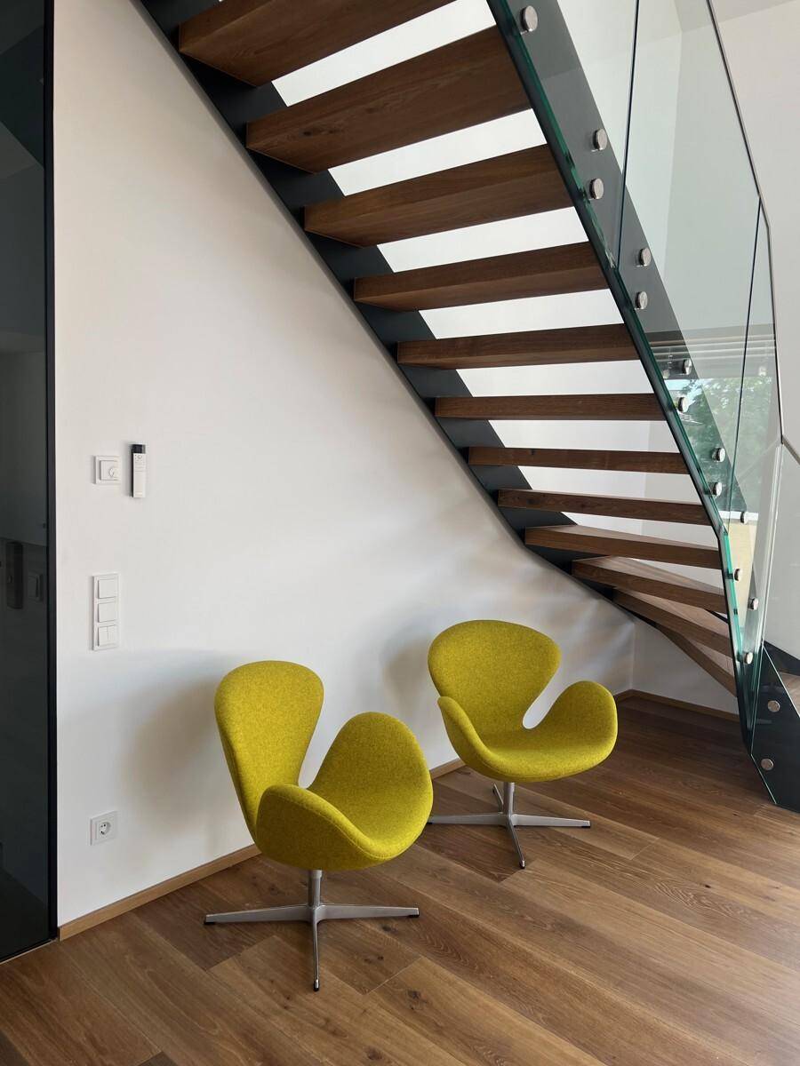 Stilvolle Holztreppe mit Glasgeländer und zwei auffälligen gelben Design-Sesseln.