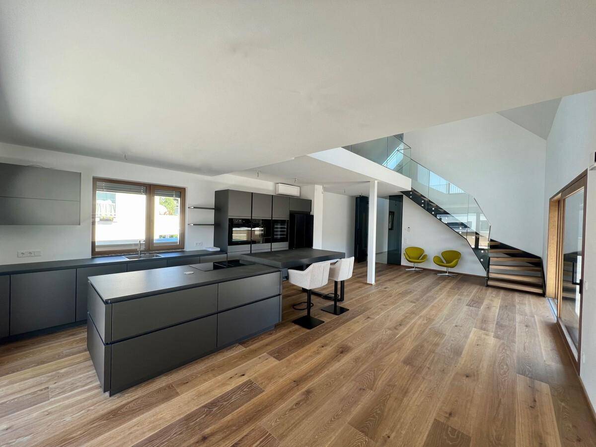 Offener Wohn- und Essbereich mit moderner Küche, Holzboden und eleganter Treppe.