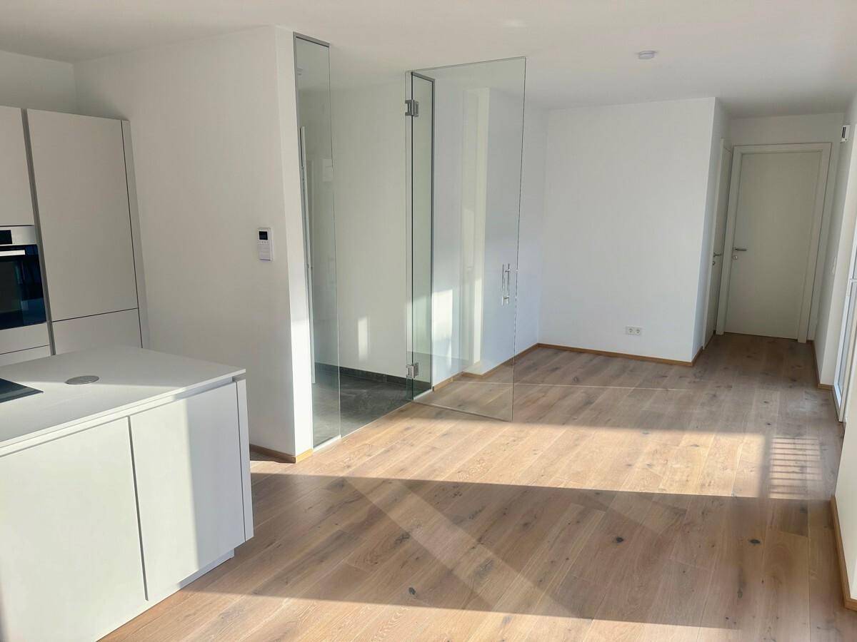 Heller offener Wohnbereich mit Holzboden, moderner Küche und eleganter Glasabtrennung.