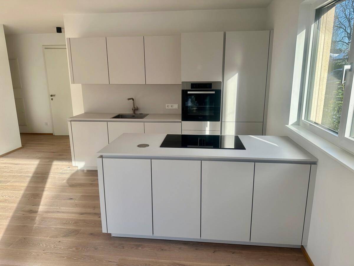Stilvolle, helle Küche mit Kücheninsel, Induktionskochfeld und integriertem Backofen.