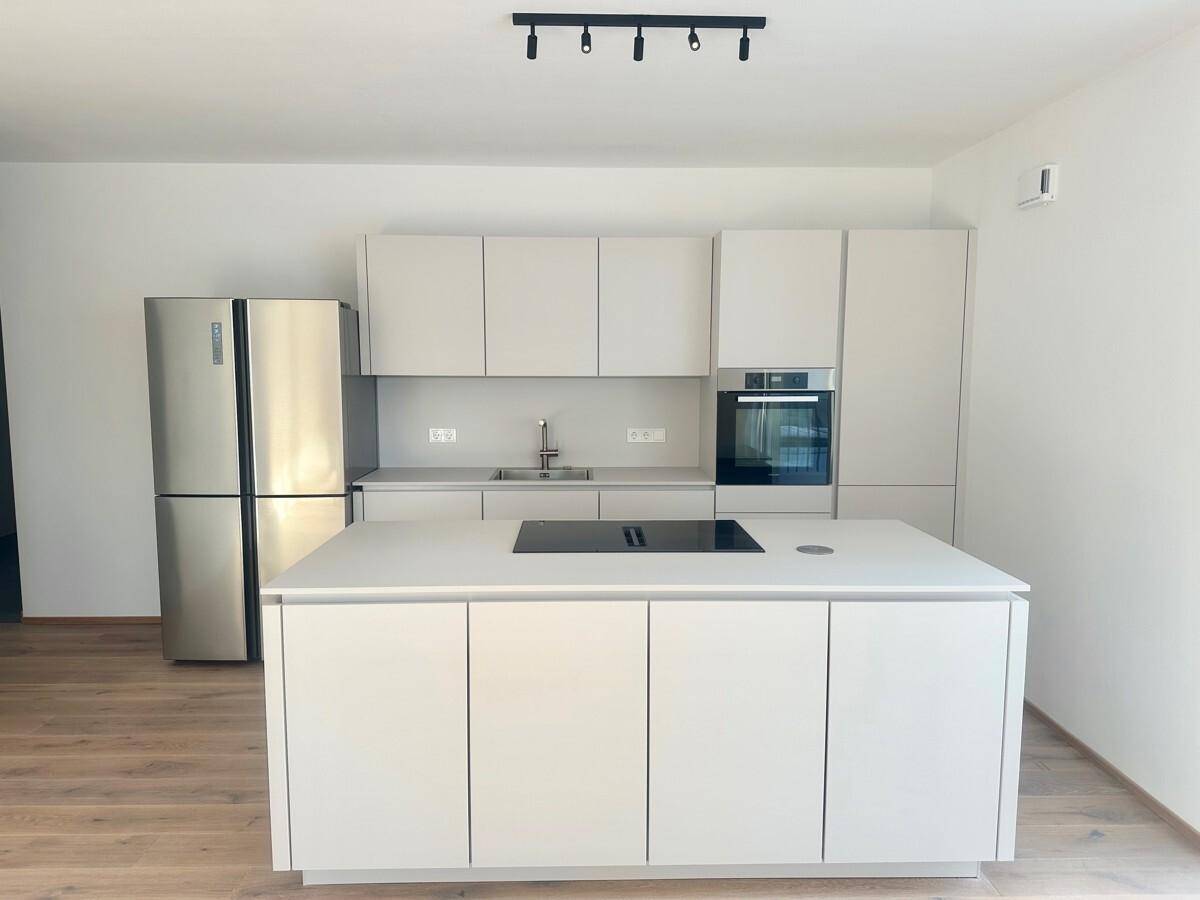 Moderne, helle Küche mit Kücheninsel, integriertem Kochfeld und Edelstahlkühlschrank.
