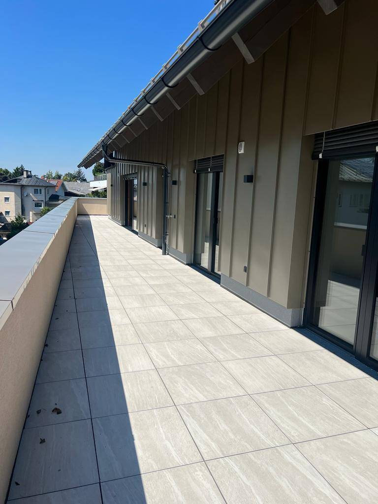 Geräumige, geflieste Dachterrasse mit viel Sonnenlicht und Blick auf die umliegenden Gebäude.