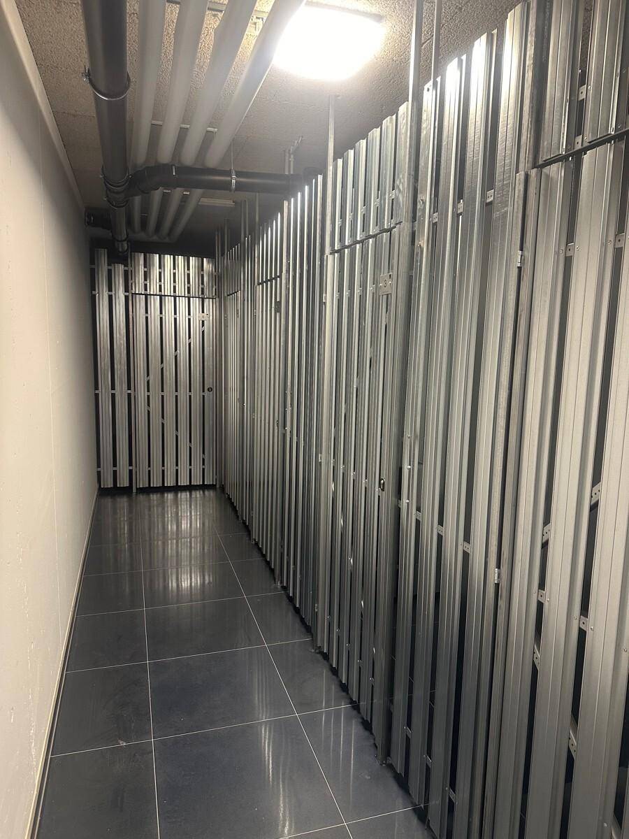 Langer Lagerraum im Keller mit Metallabtrennungen und Fliesenboden.