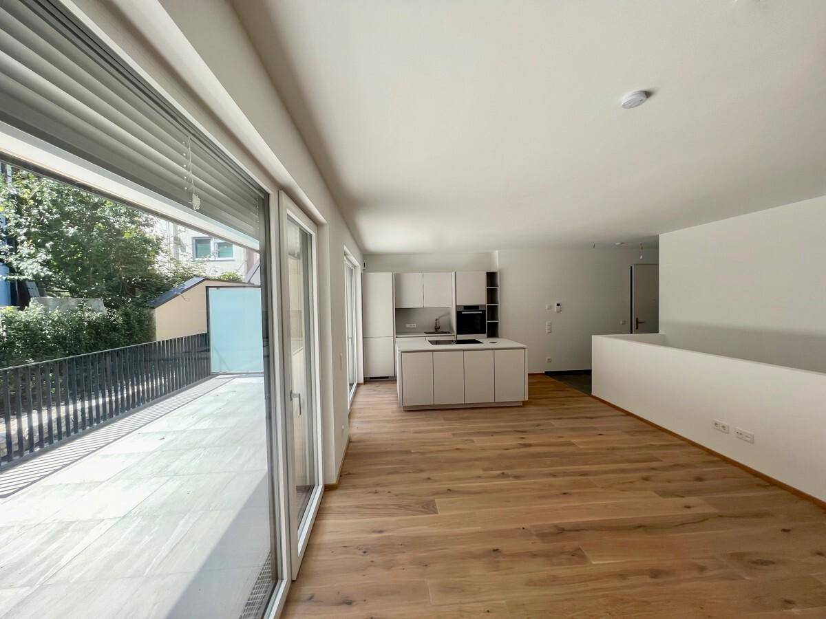 Offener Wohnbereich mit Holzboden, moderner Küche und großen Fenstern zur Terrasse.