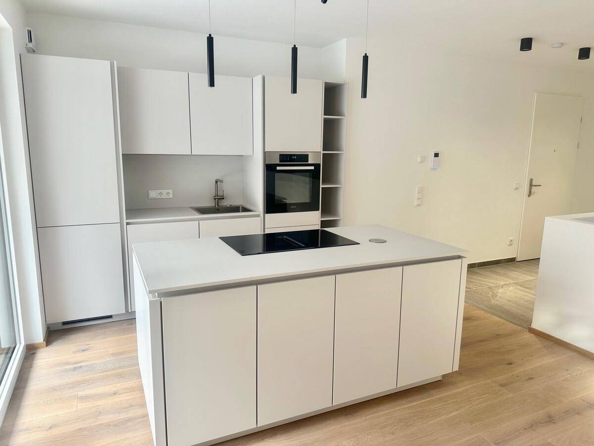 Moderne Küche mit Kücheninsel, Induktionskochfeld und stilvollen schwarzen Pendelleuchten.