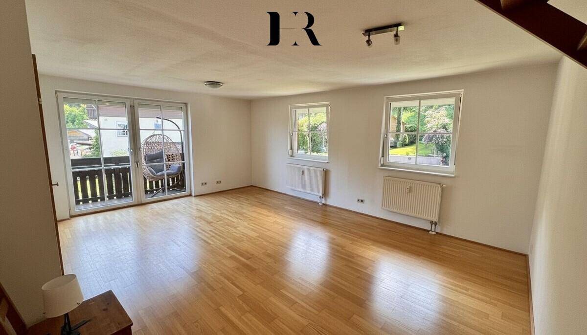 Helles Wohnzimmer mit Parkettboden, weißen Wänden und direktem Zugang zu einem Balkon.