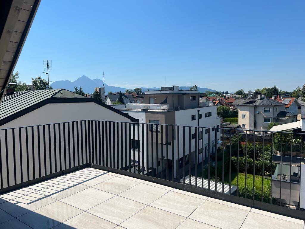 Sonniger Terrassenbereich mit modernem Geländer und weitem Blick auf die Berge und die Stadt.