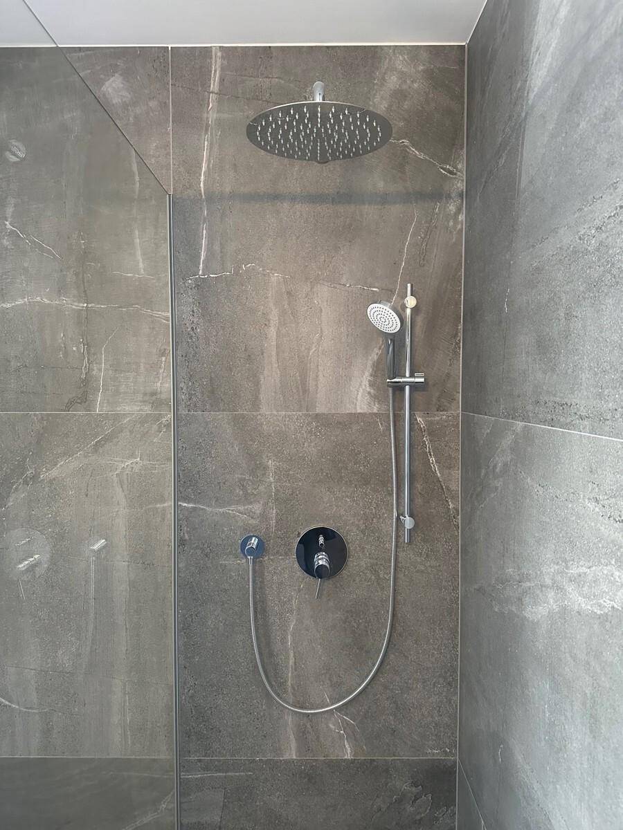 Duschbereich mit großer Regendusche und Handbrause an dunkelgrauen Fliesenwänden.