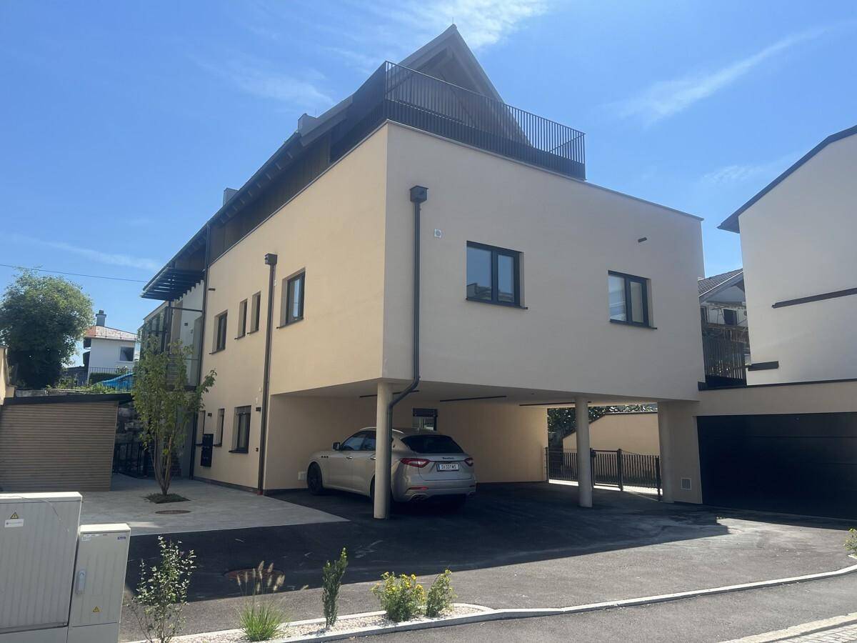 Ansicht des modernen Gebäudes mit Carport und gepflegter Zufahrt an einem sonnigen Tag.