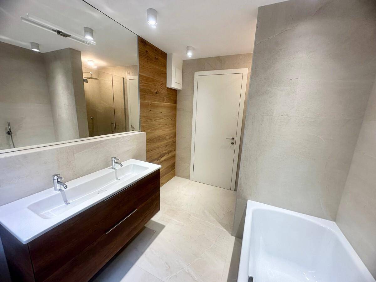 Helles Badezimmer mit Doppelwaschbecken, großem Spiegel und integrierter Badewanne.